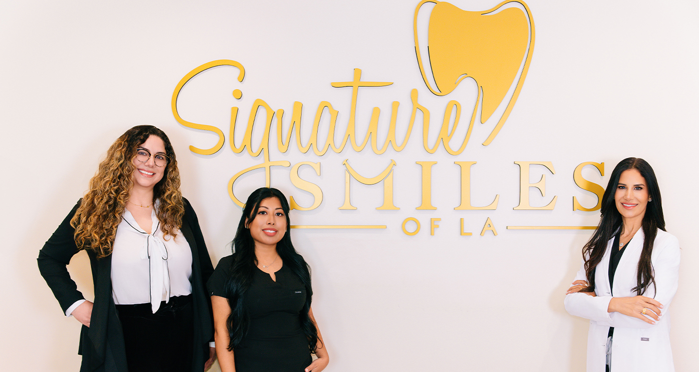 Encino dentist and two team members smiling in front of a Signature Smiles of LA sign